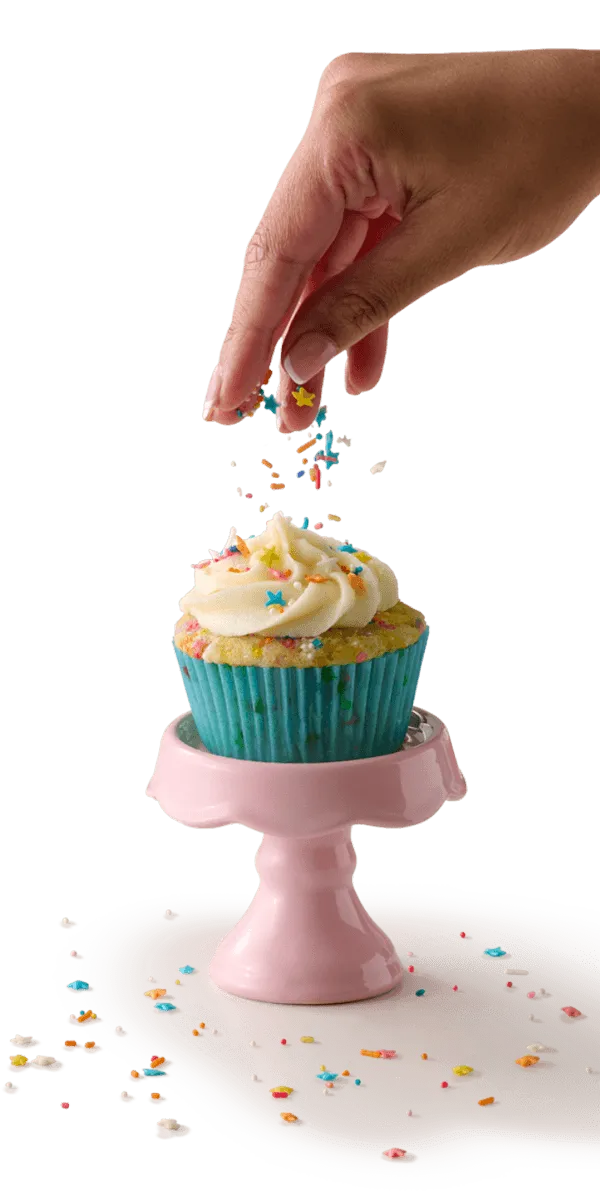 Hand dropping sprinkles onto cupcake