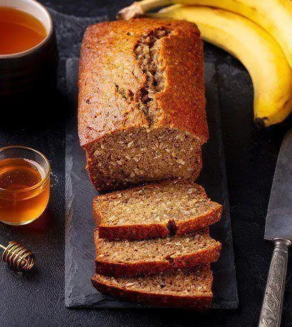 Sliced banana loaf on slab with honey in a cup